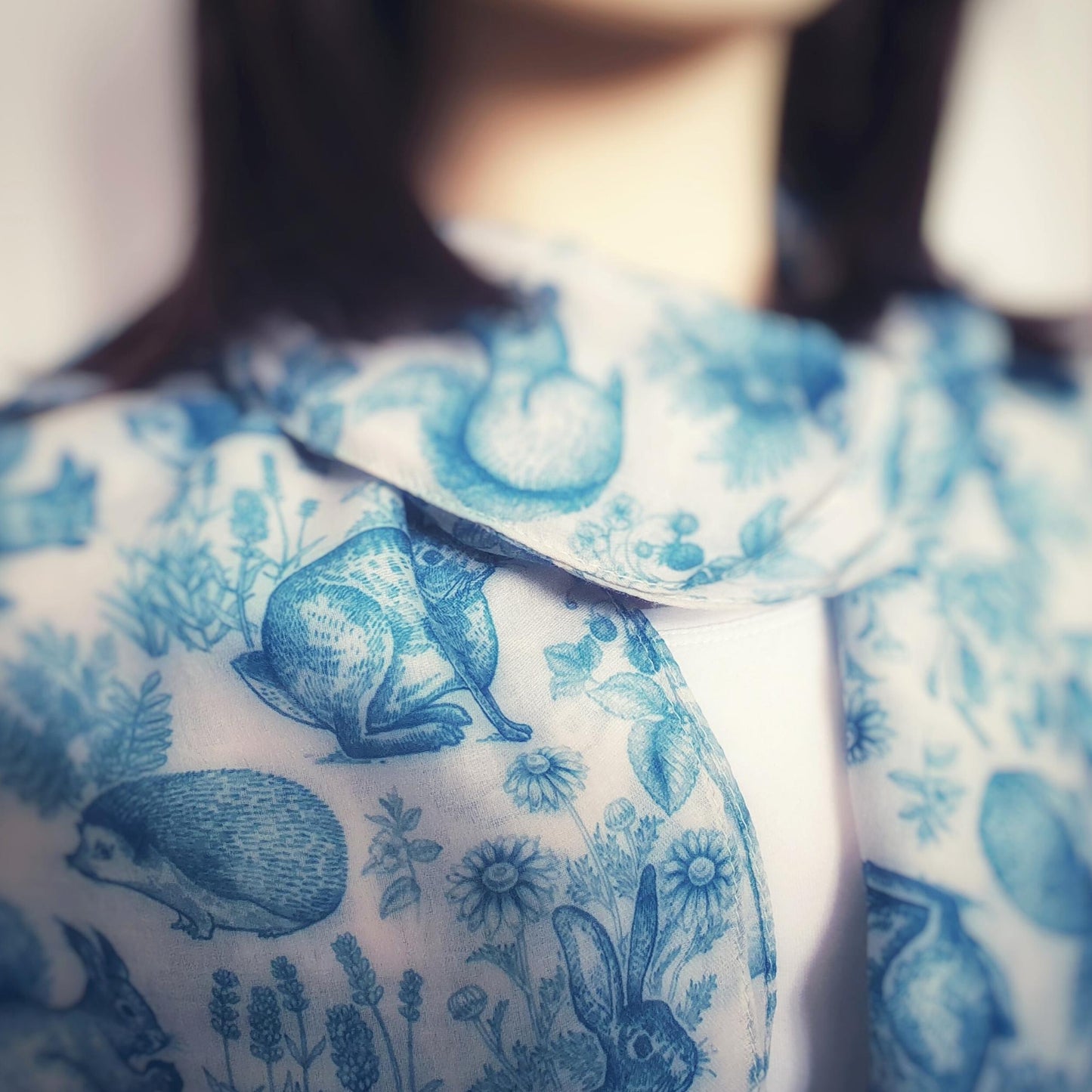 Close-up of a person wearing blue floral woodland animal scarf on a blurred background