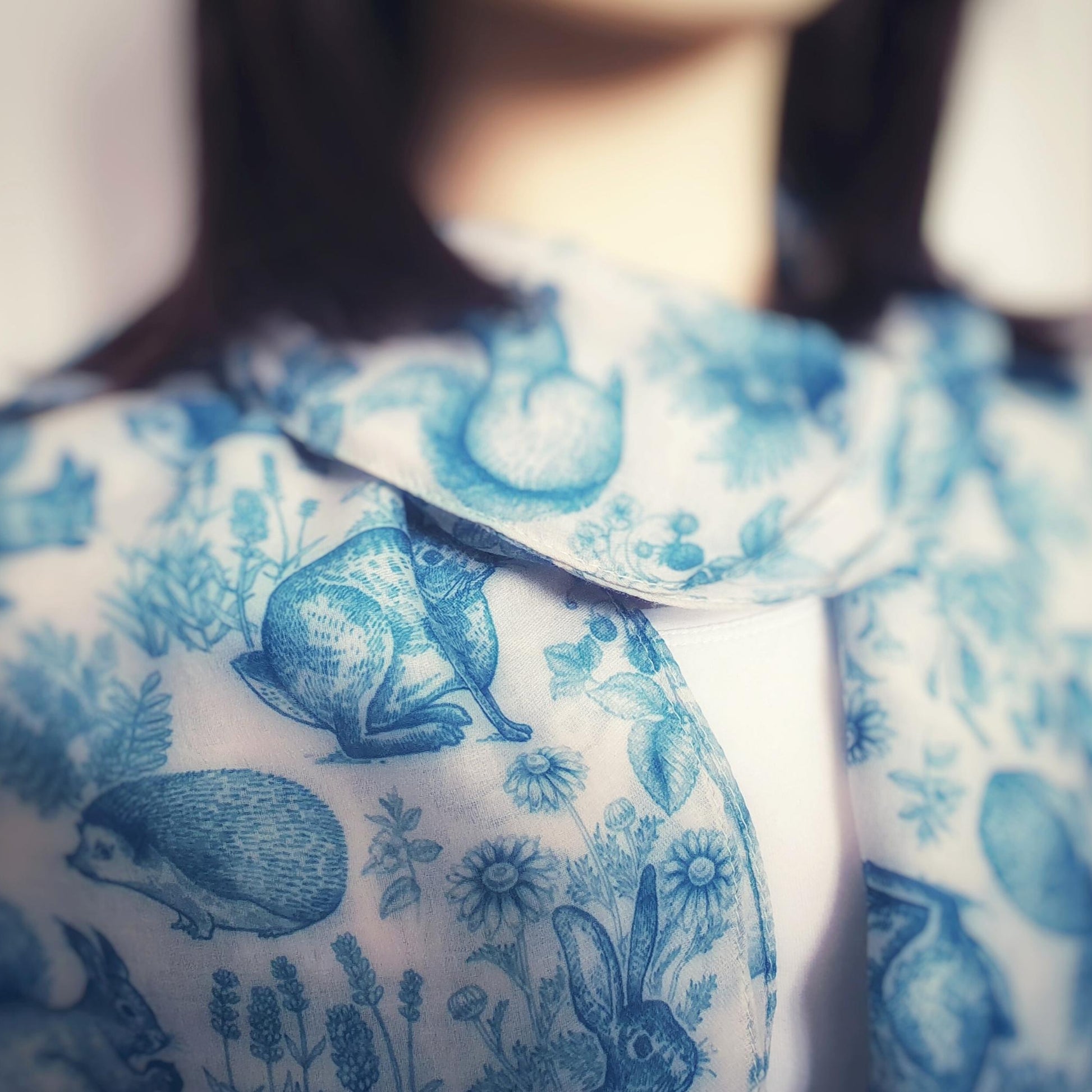Close-up of a person wearing blue floral woodland animal scarf on a blurred background