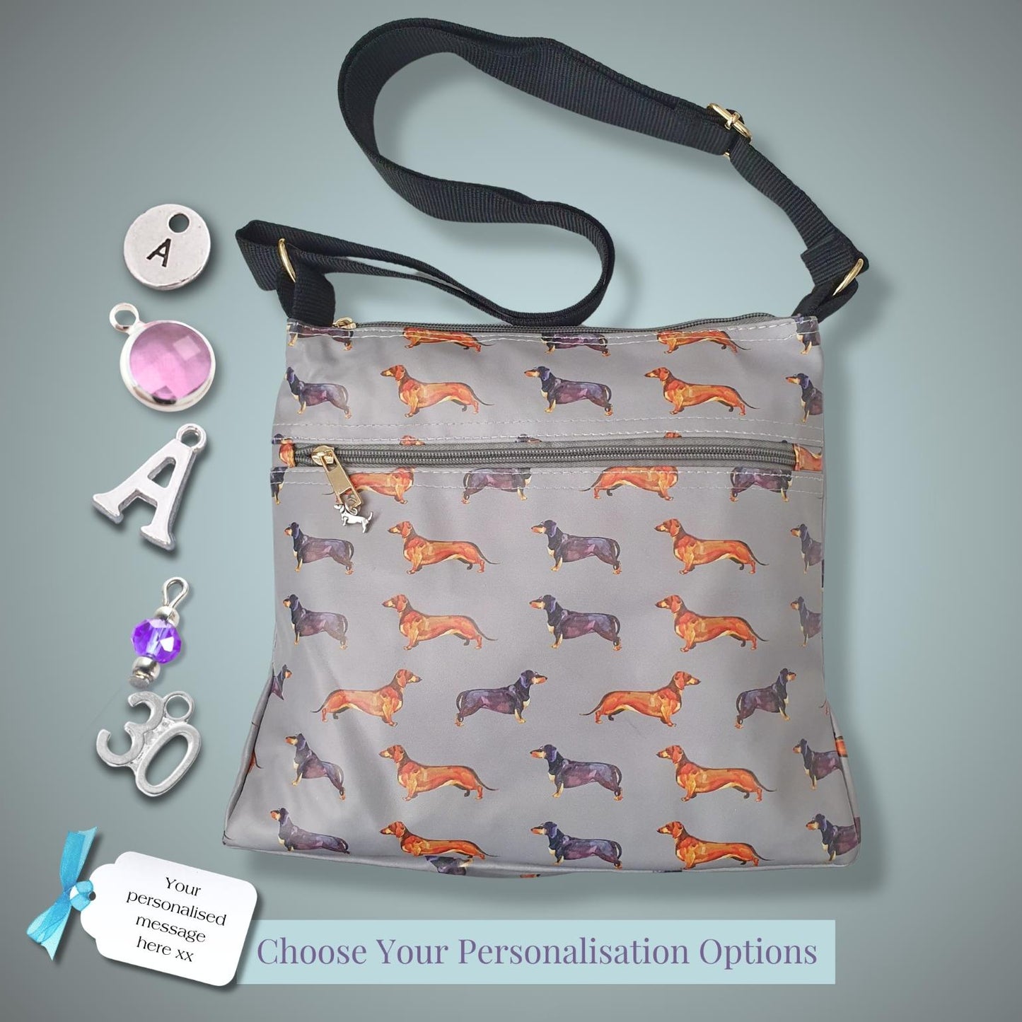 A grey crossbody bag with an orange and brown dachshund pattern, shown with various personalization options like initial letters, charms, and a text tag on a grey gradient background.