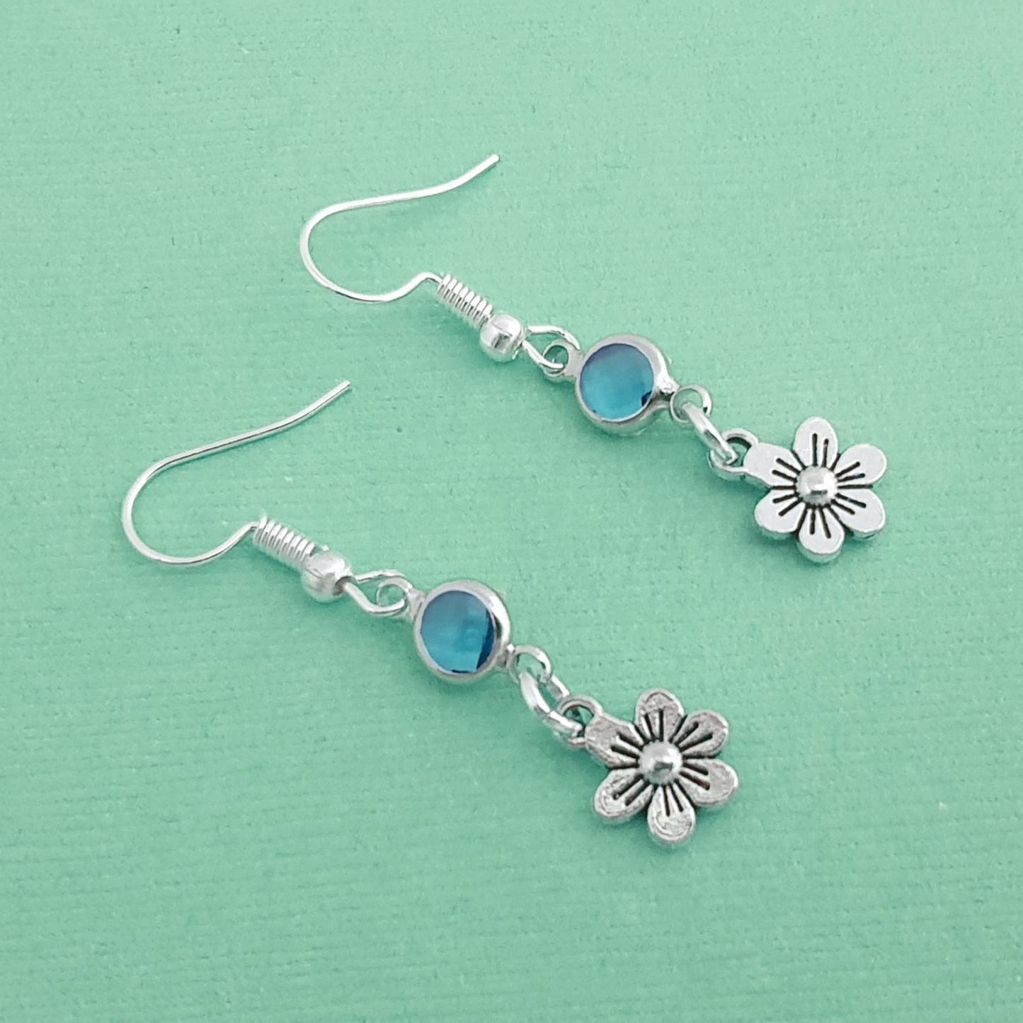 Silver earrings with flower charms on a light green background