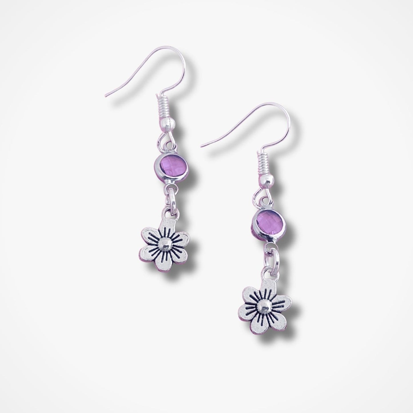 Silver earrings with purple beads and flower charms on a white background