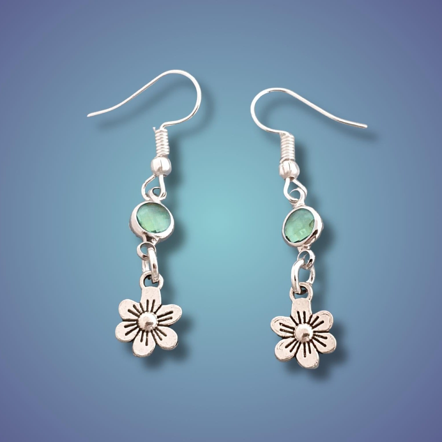 Silver earrings with flower charms on a gradient blue background