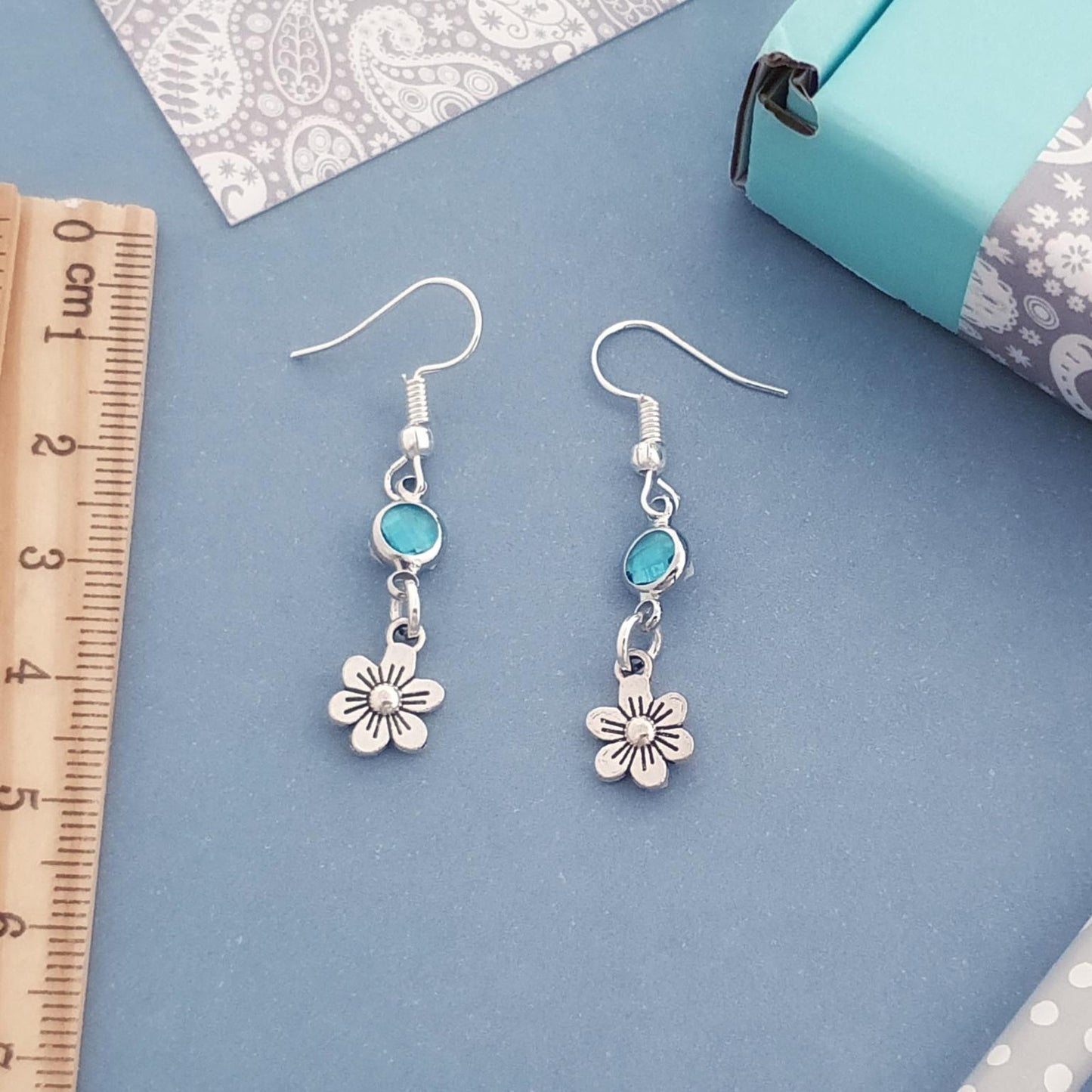 Silver flower-shaped earrings with turquoise stones on a blue surface with a ruler for scale.