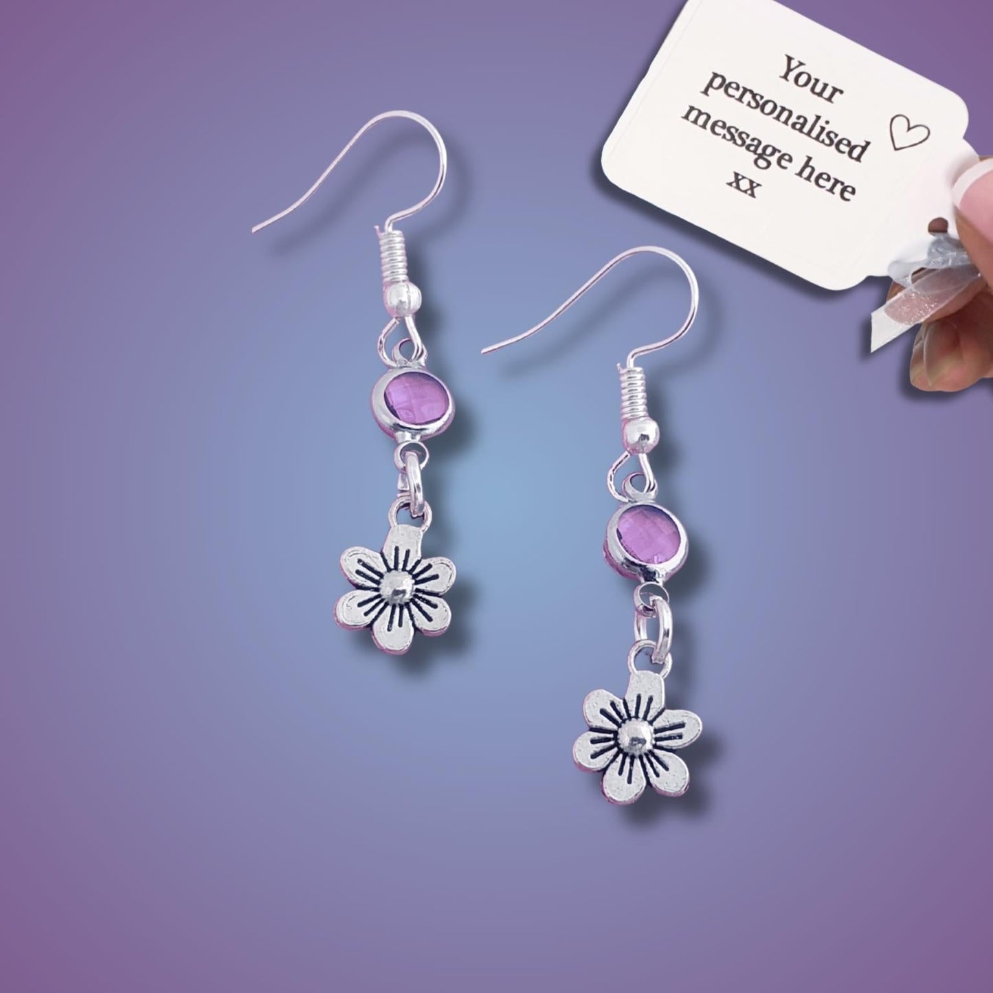 Silver earrings with purple beads and flower charms on a purple background