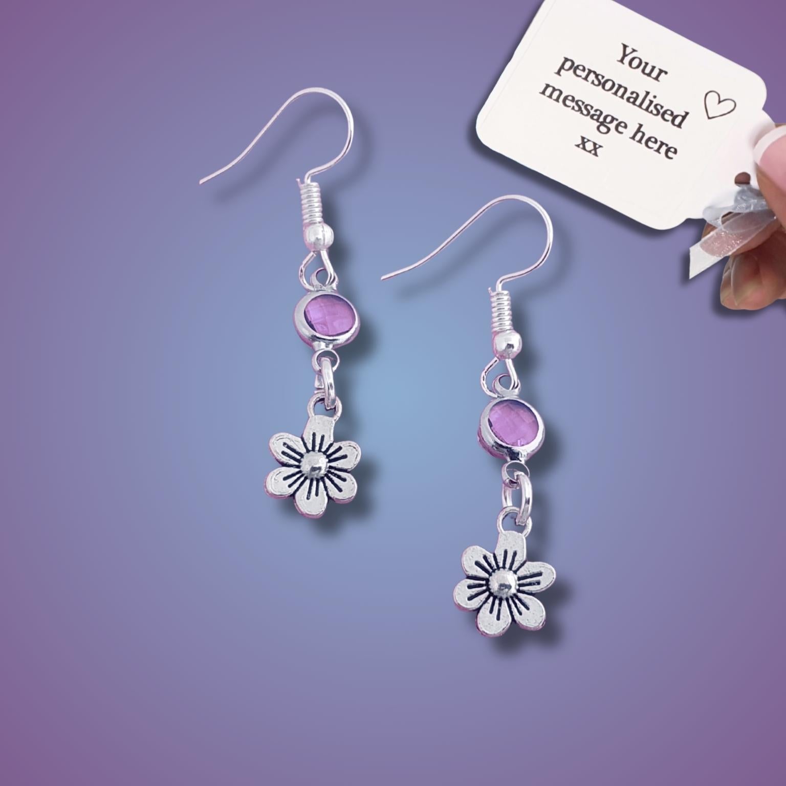 Silver earrings with purple beads and flower charms on a purple background