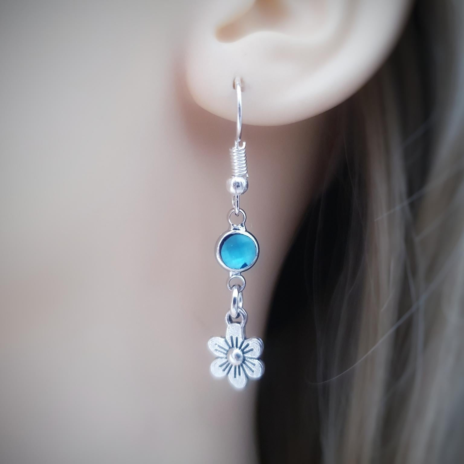 Earring with blue gemstone and flower charm worn by a person.