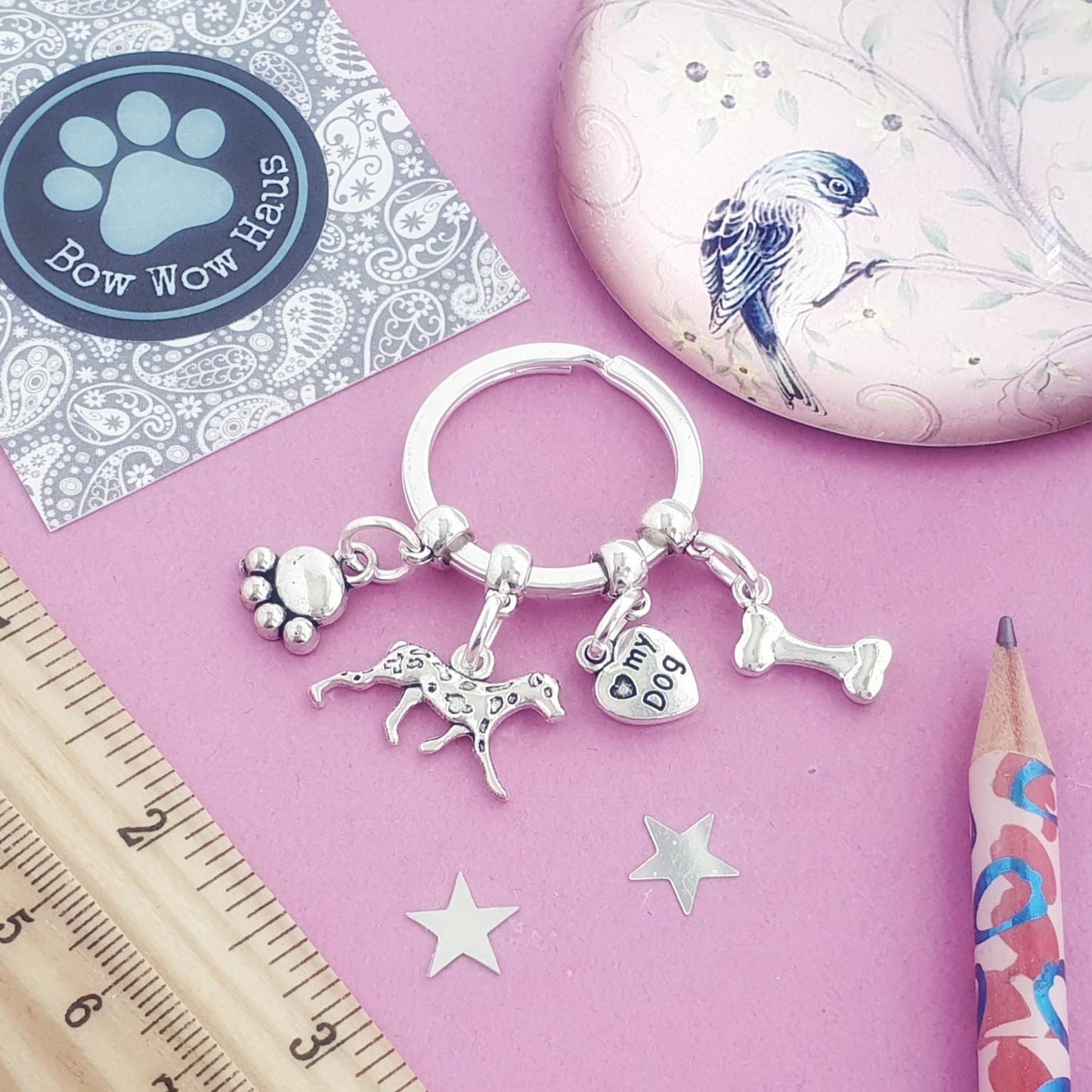 Keychain with paw, dalmatian, and bone charms on a pink surface with a ruler and pencil.