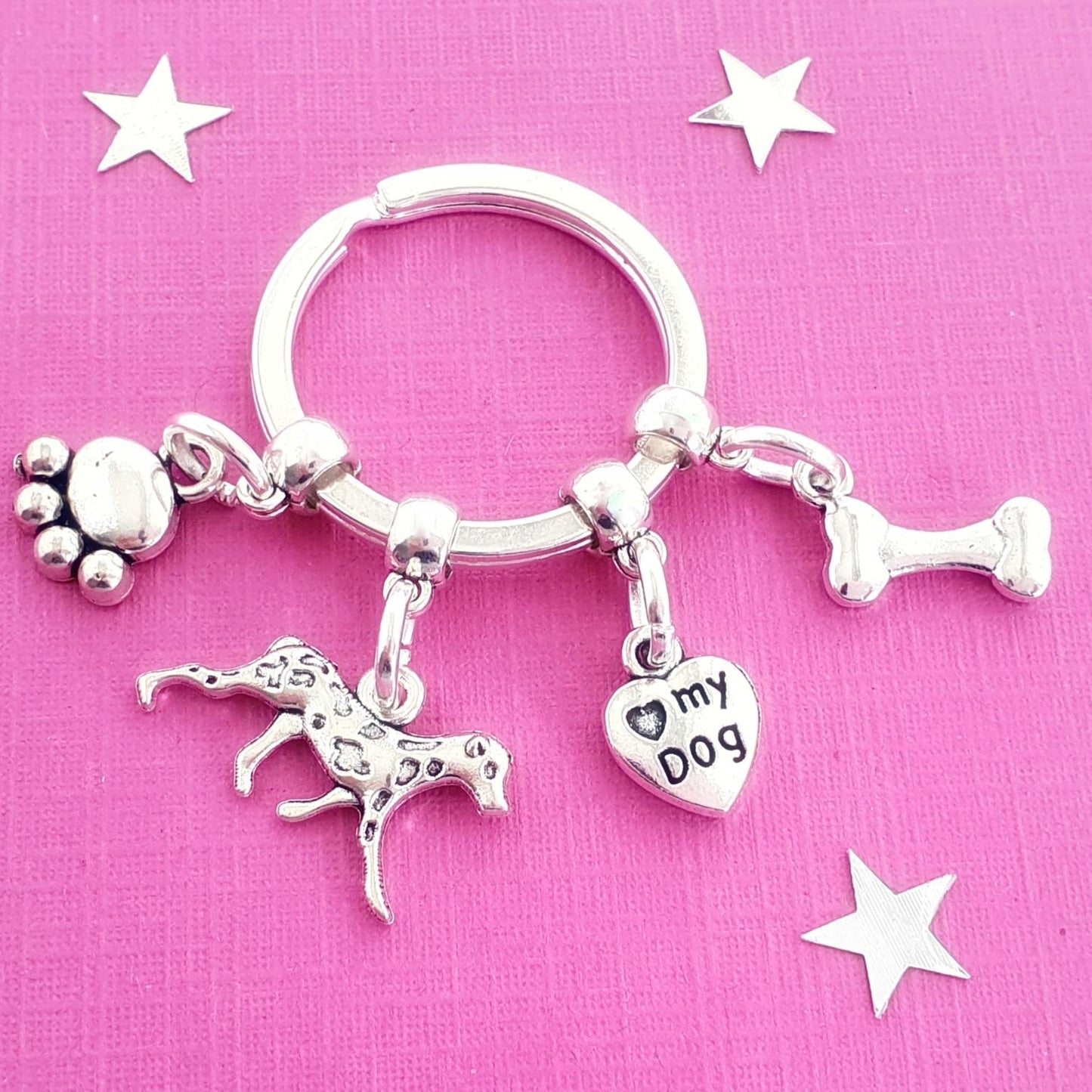 Silver keychain with dog-themed charms on a pink background with star decorations