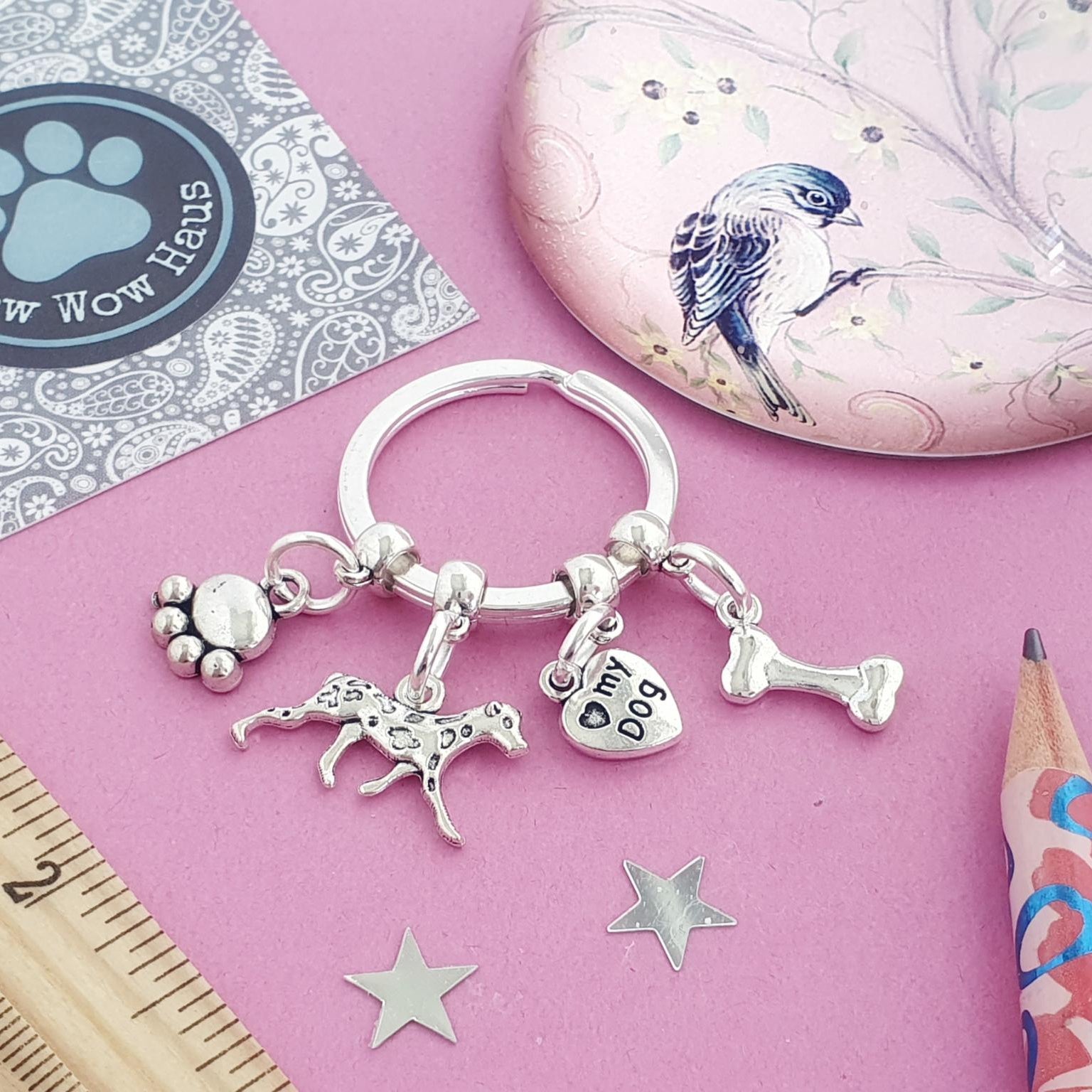 Keychain with paw, dalmatian, and bone charms on a pink surface with stationery items