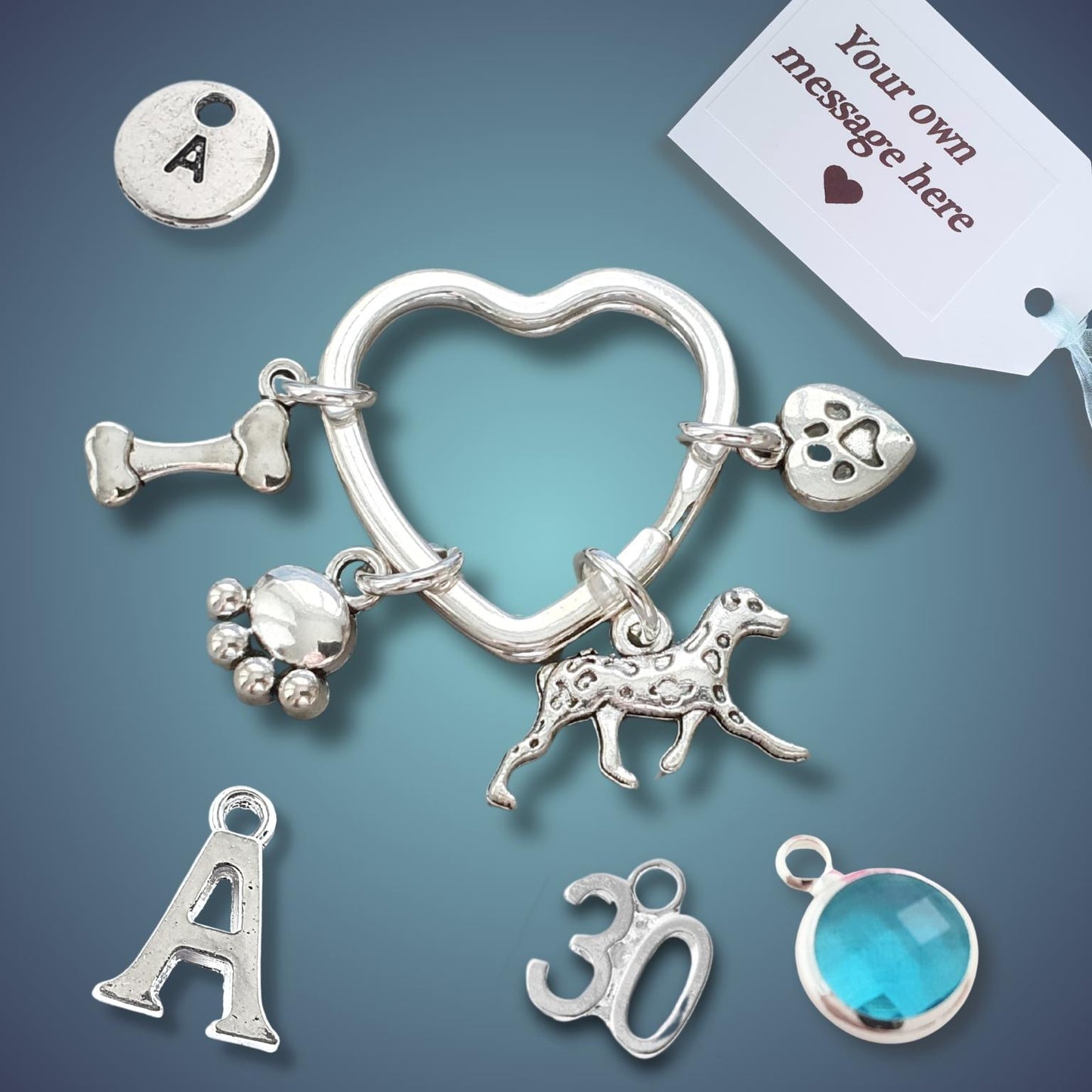 A set of silver charms for jewelry making, featuring a heart-shaped ring, a dog silhouette, a paw print, a bone, a paw pad, a round letter 'A' charm, a '30' charm, and a blue gemstone bezel, displayed on a dark blue gradient background with a white customization tag.