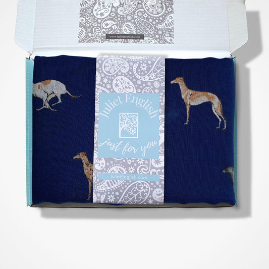 A navy blue scarf with greyhound dog illustrations, presented in an open gift box with a Juliet English band.