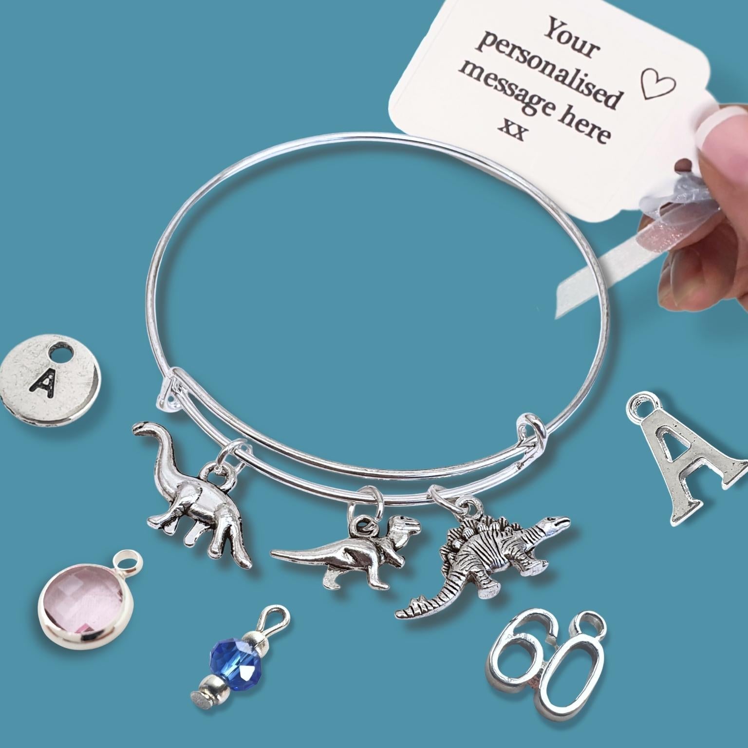 Silver bracelet with dinosaur charms and a personalized message tag on a blue background