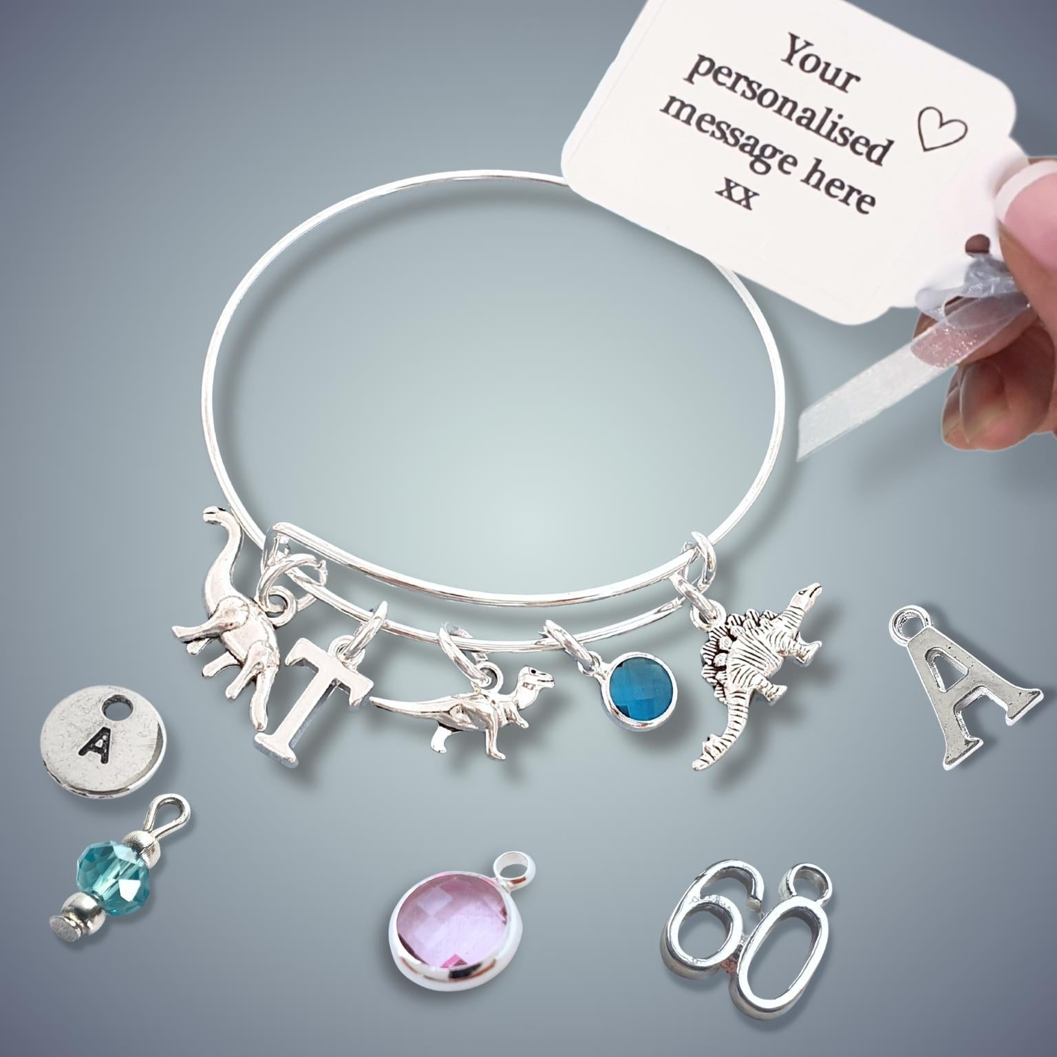 Silver bracelet with various charms and a personalized message card on a gray background