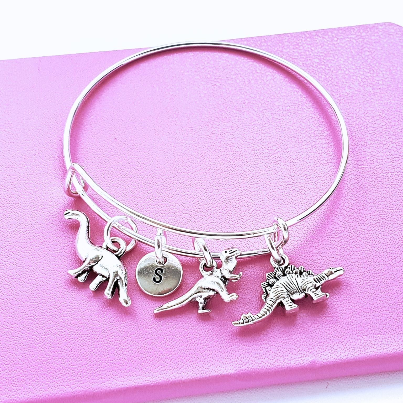 Silver bracelet with dinosaur charms on a pink background
