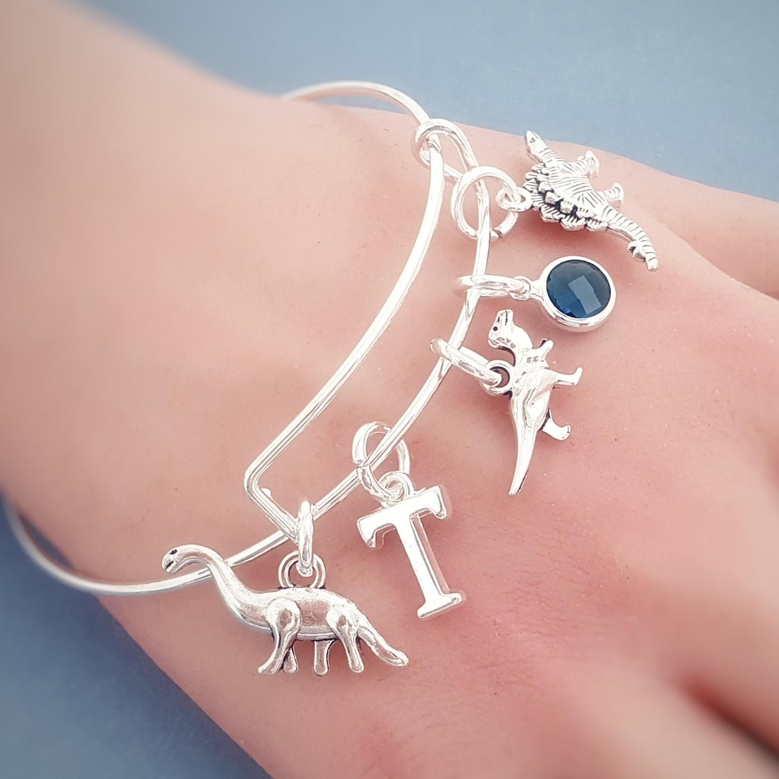 Silver bracelet with various charms on a hand against a light blue background