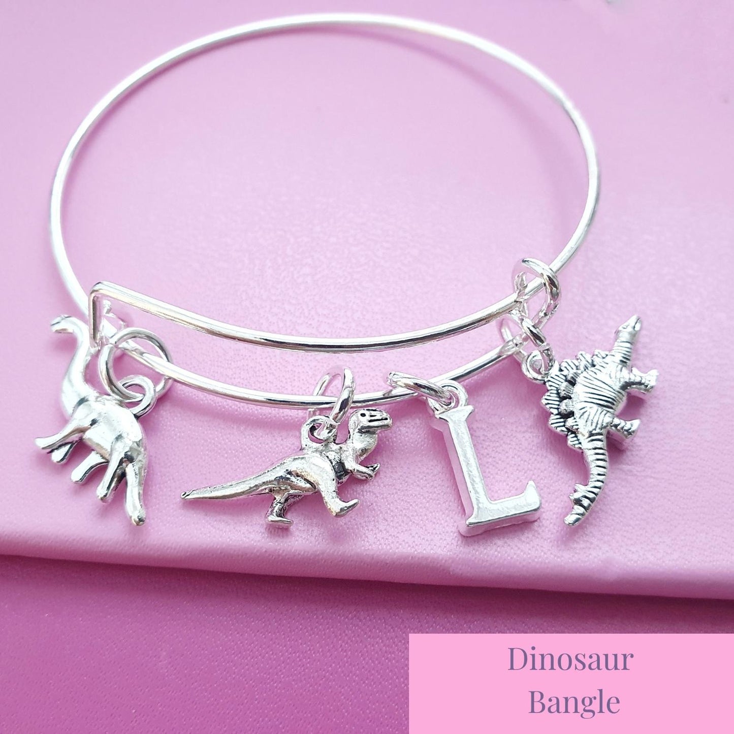 Silver dinosaur bangle with charms on a pink background