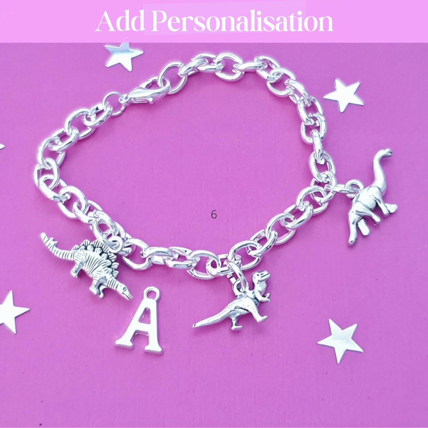 A silver chain bracelet with dinosaur charms and a letter 'A' charm, displayed on a pink background with decorative star cutouts and the text 'Add Personalisation' at the top.