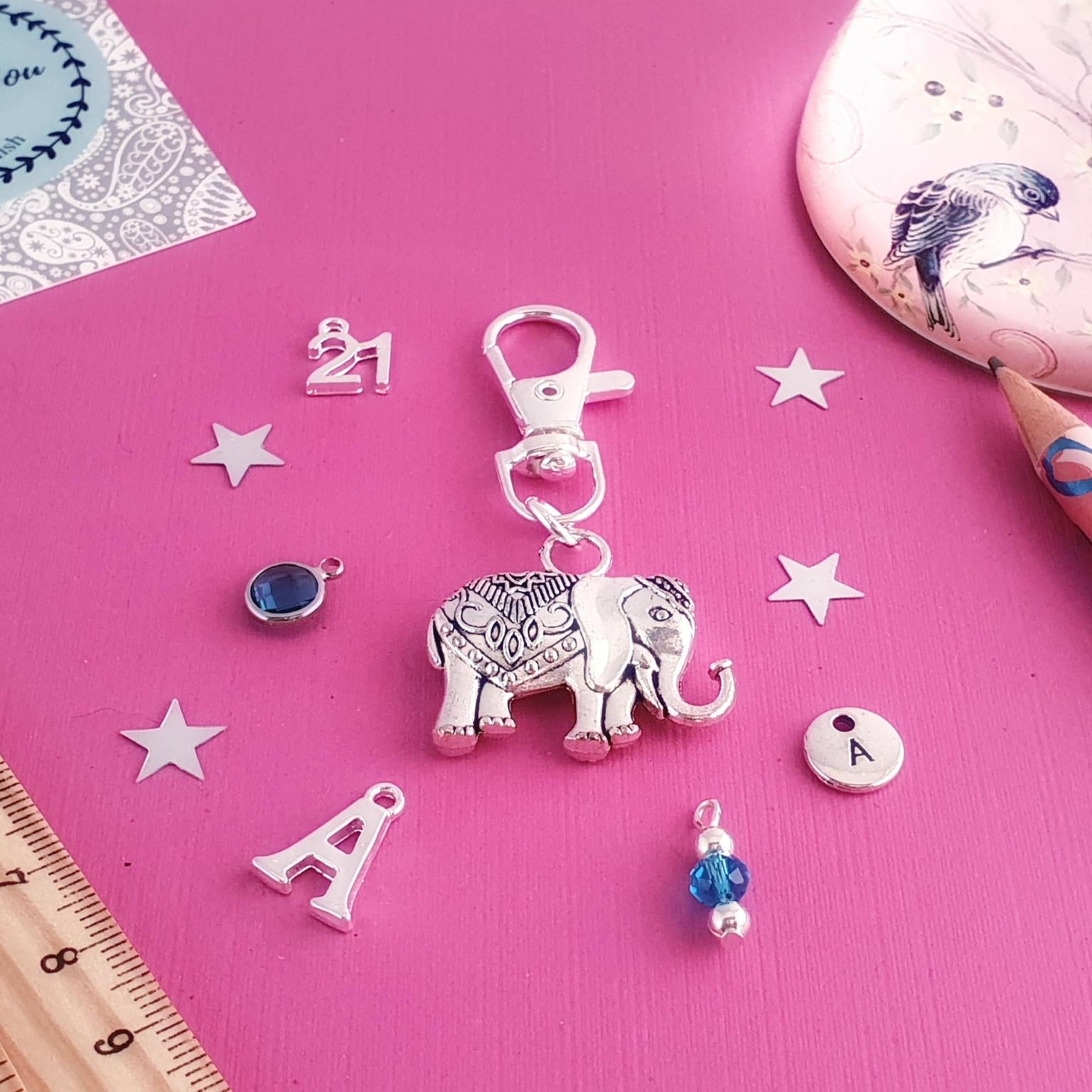 Decorative elephant keychain with charms on a pink surface with stationery items.