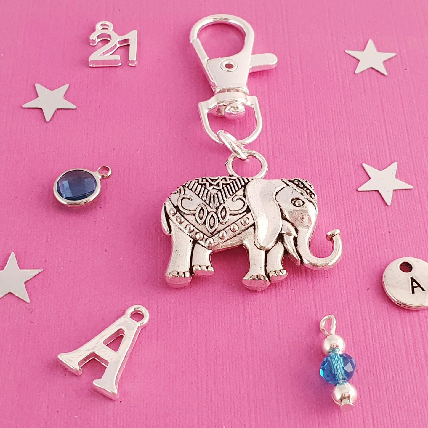Silver elephant keychain with decorative elements on a pink background