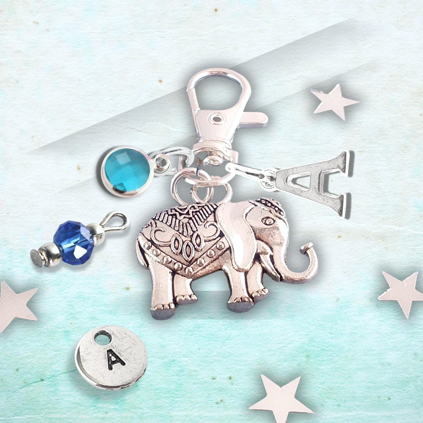 Silver charm with elephant design and blue gemstone on a light blue background with stars