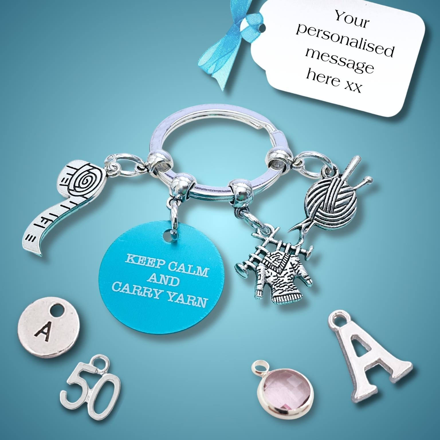A silver-toned keyring charm set displayed on a blue gradient background, featuring a round turquoise charm that reads 'KEEP CALM AND CARRY YARN,' a knitting needle and yarn motif, a small figure charm, and several letter and number charms. A white tag at the top says 'Your personalised message here xx.