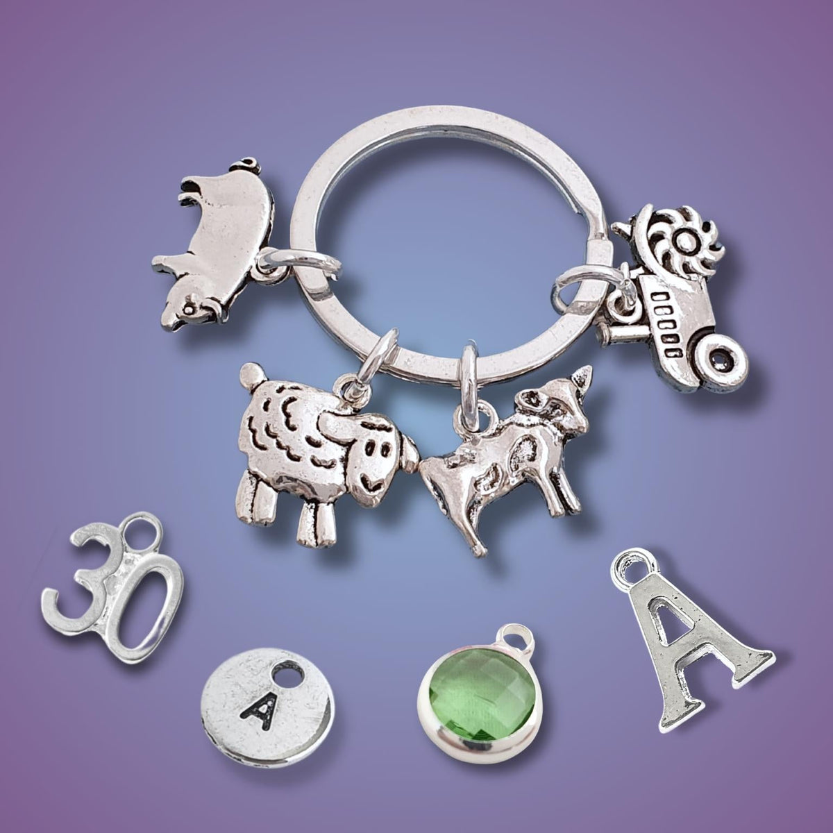 A silver tone charm key ring with various animal and letter charms, including a sheep, a pi, a cow, a tractor, and letters A, 30, and a green gemstone, displayed on a purple gradient background.