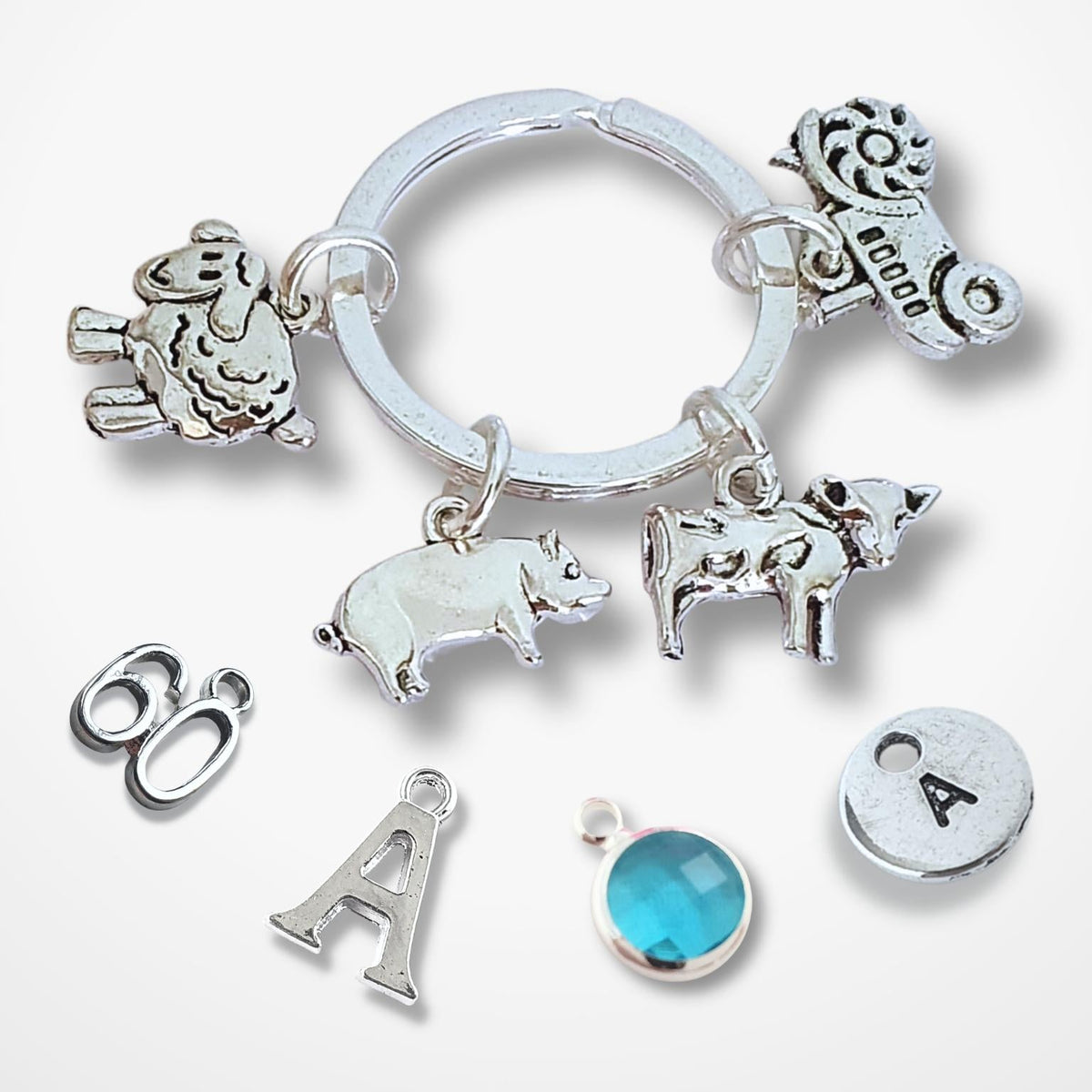 A silver tone charm key ring with various animal and letter charms, including a sheep, a pi, a cow, a tractor, on a light gray background.