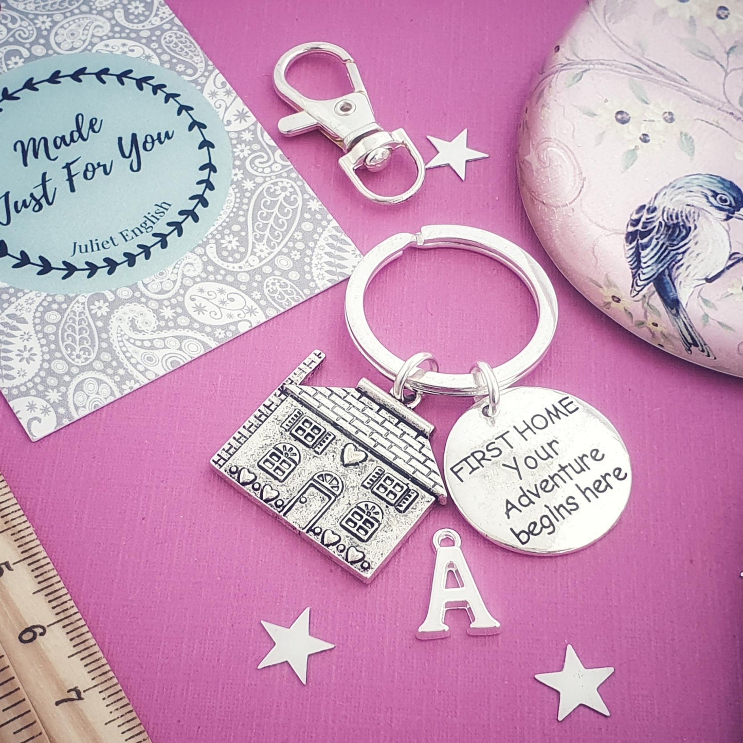 Silver keychain with engraved text on a pink surface with decorative elements.