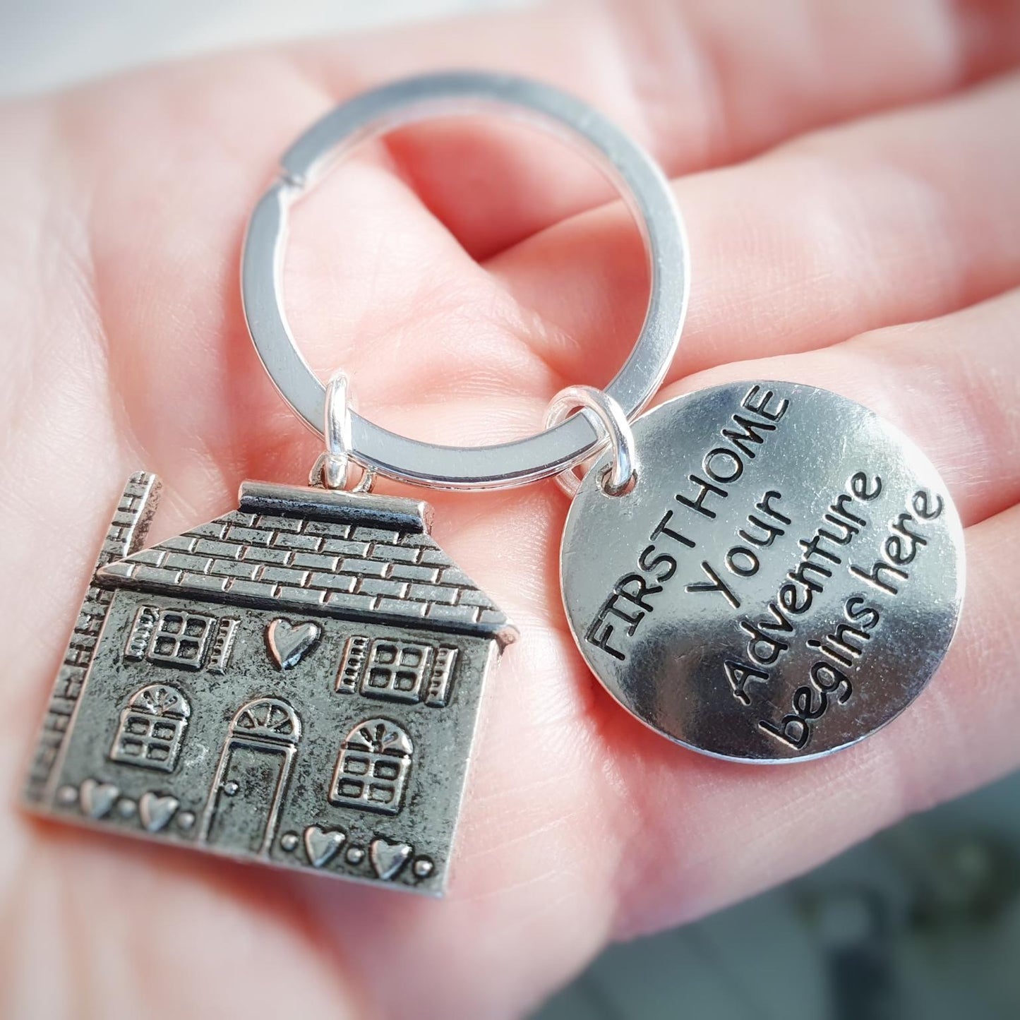 Keychain with house charm and 'First Home, Your Adventure Begins Here' tag held in a hand.