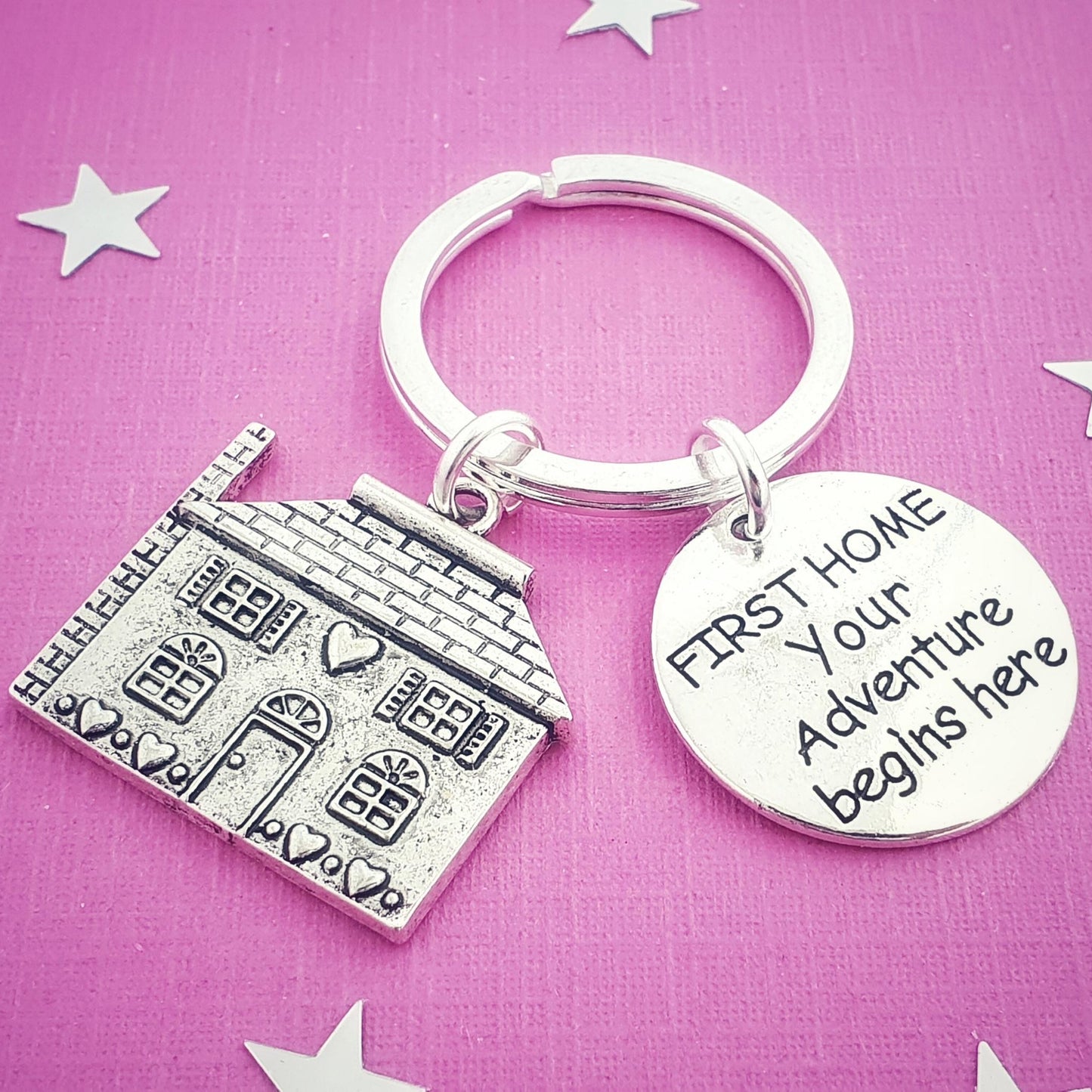 Keychain with house charm and 'First Home Your Adventure Begins Here' tag on a pink background