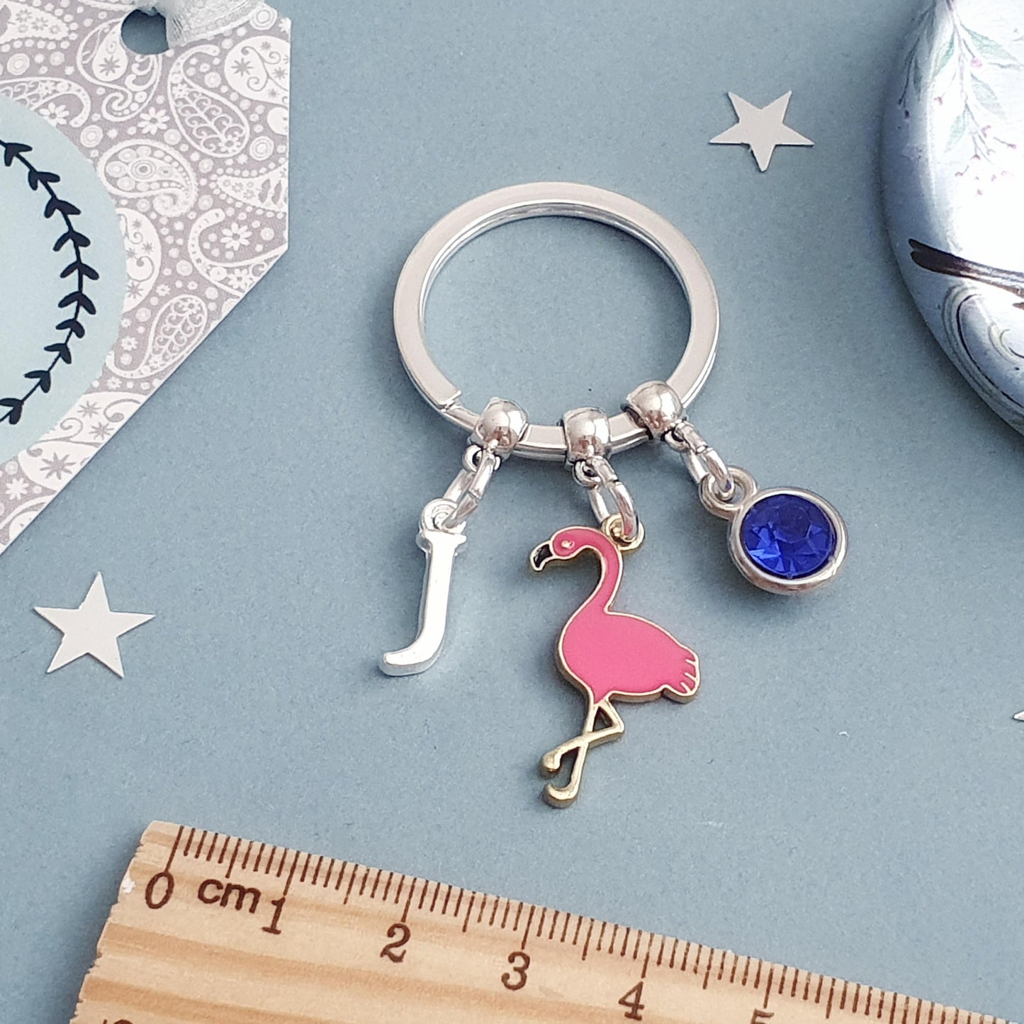 Keychain with flamingo charm and optional letter and birthstone charms on a blue background with stars and a decorative tag.