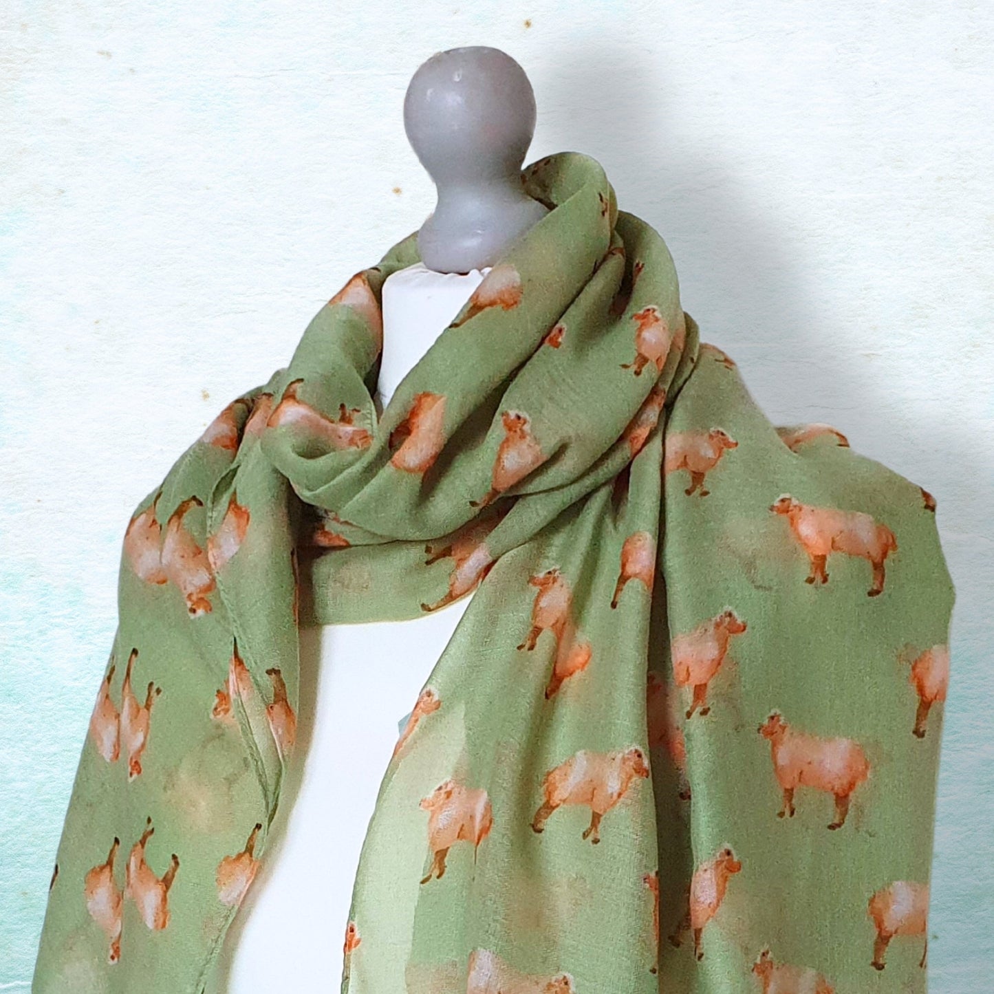 Green scarf with sheep pattern on a mannequin against a light blue background