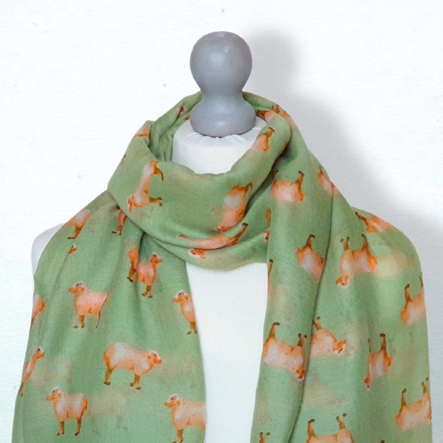 Green scarf with sheep pattern on a mannequin against a white background