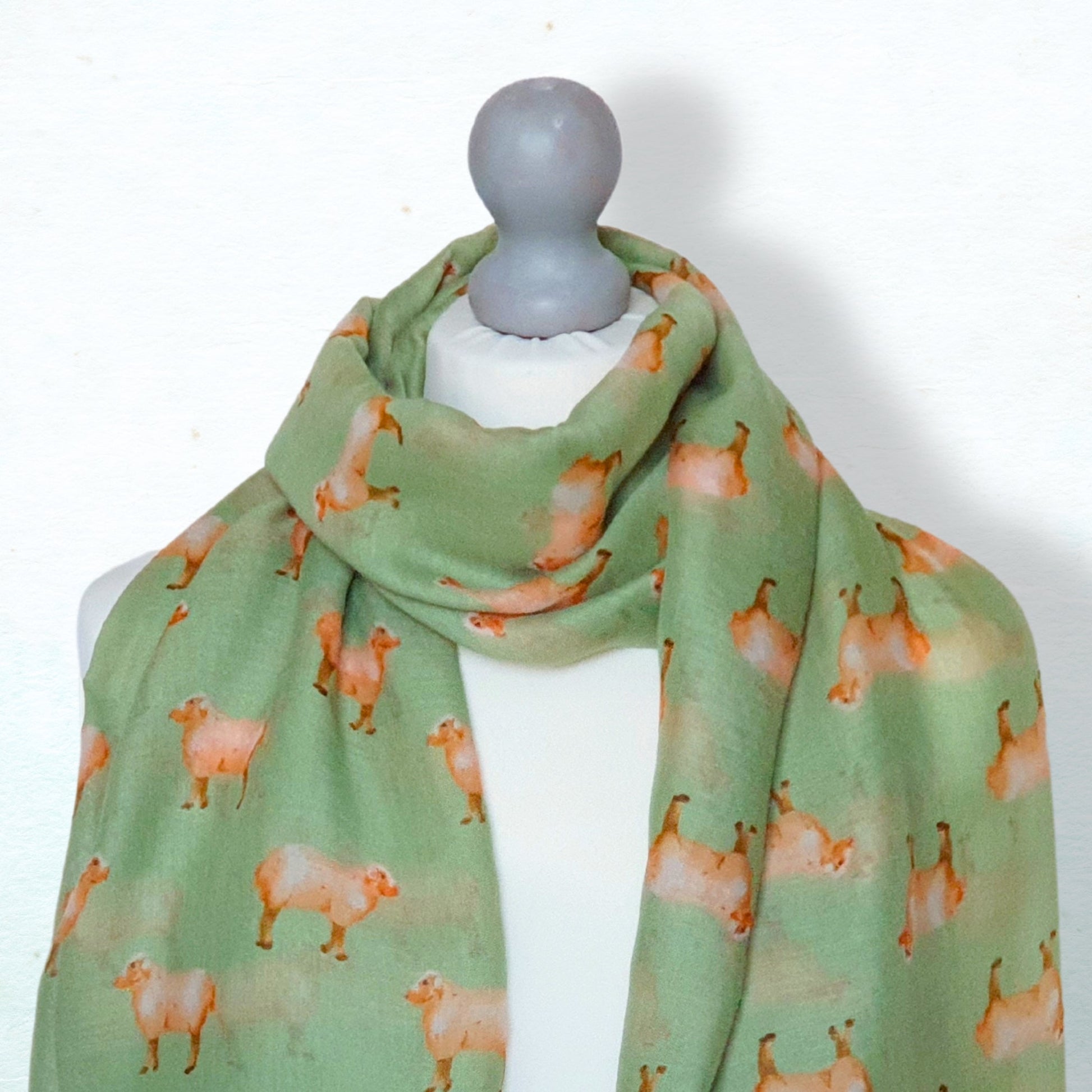 Green scarf with sheep pattern on a mannequin against a white background