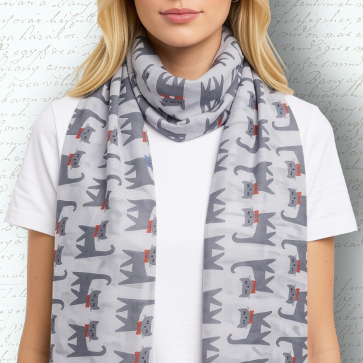 A woman wearing a light grey scarf with a repeating pattern of dark grey stylized letters and small orange-red bow ties, styled over a white t-shirt against a cursive script background.