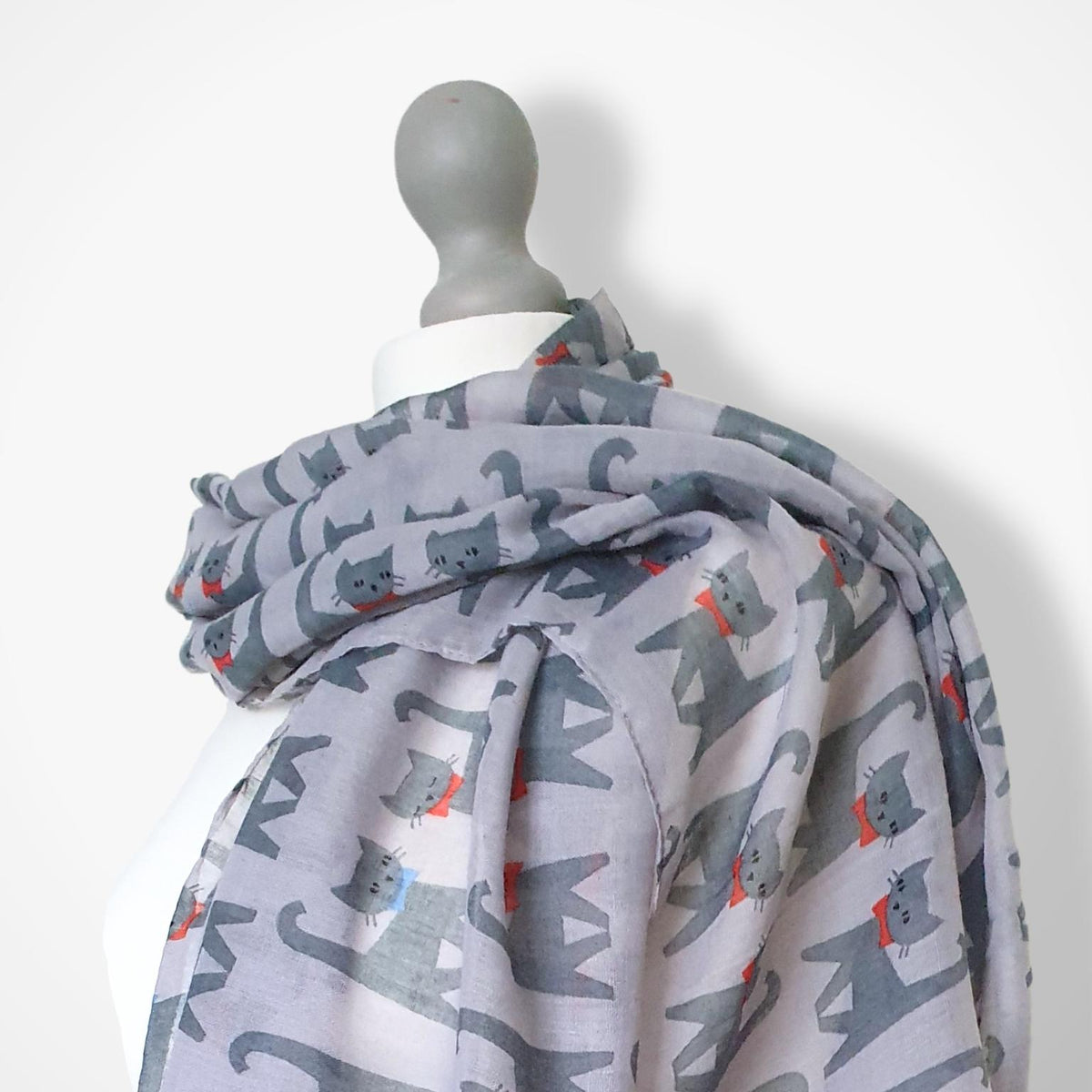A lightweight grey scarf with a playful cartoon cat pattern, draped over a mannequin torso against a plain white background.