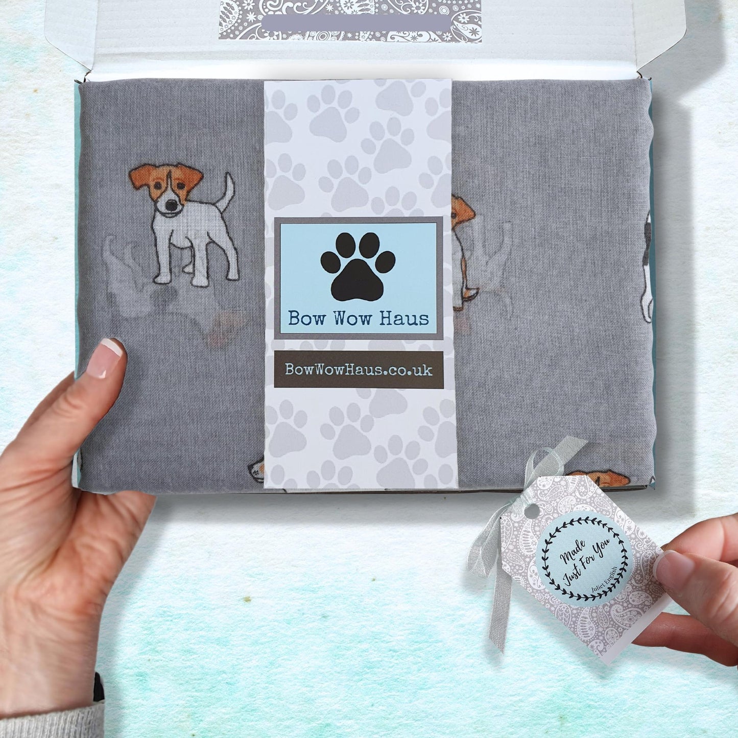 Grey scarf with jack russell dog illustrations and box with 'Bow Wow Haus' branding, held by a hand.