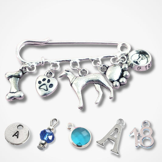 A silver charm brooch featuring a dog silhouette, paw prints, a bone, and a top dog bowl charm, displayed alongside five additional loose silver charms and a blue crystal charm on a light gray background.