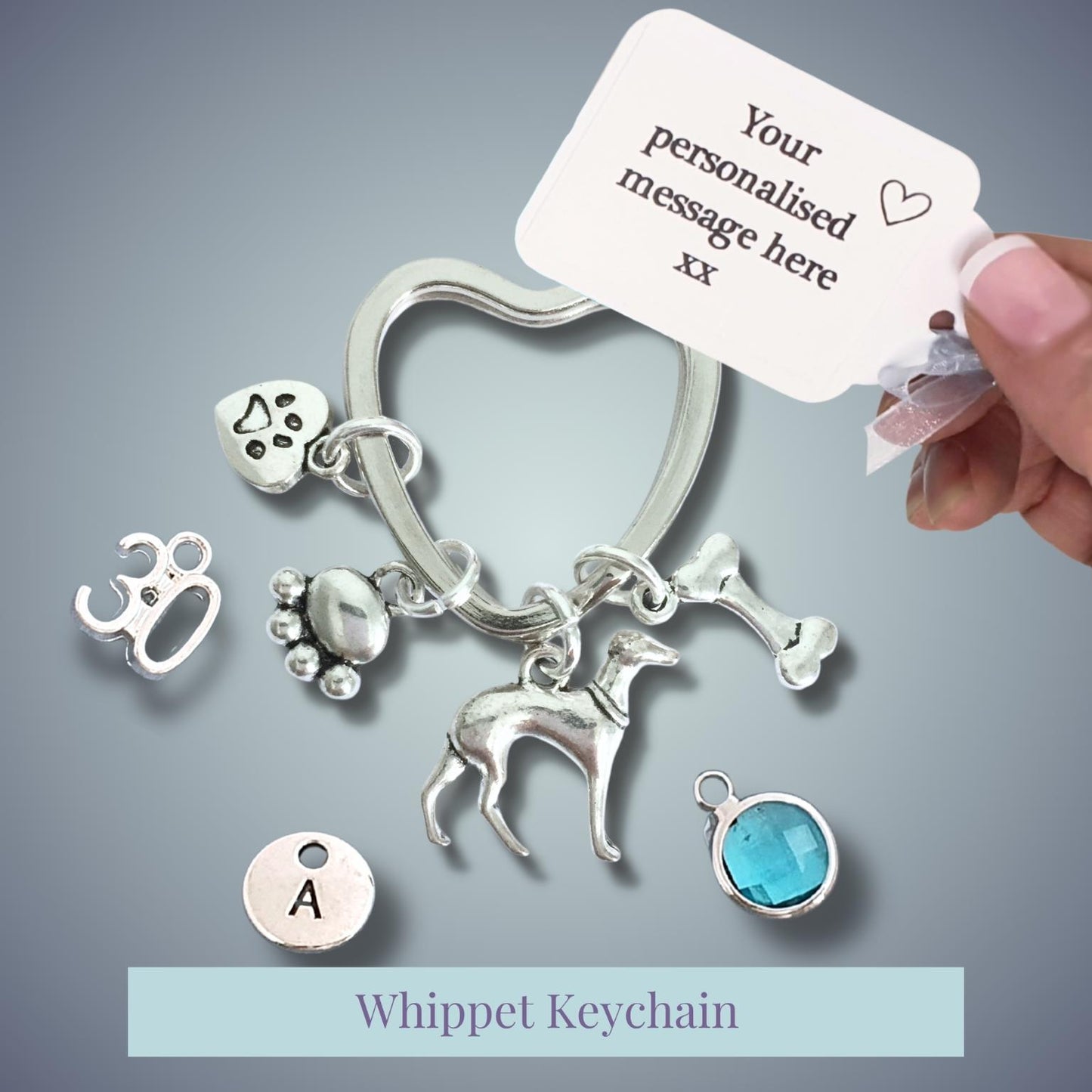 Silver whippet keychain with charms and a customizable tag on a gray background