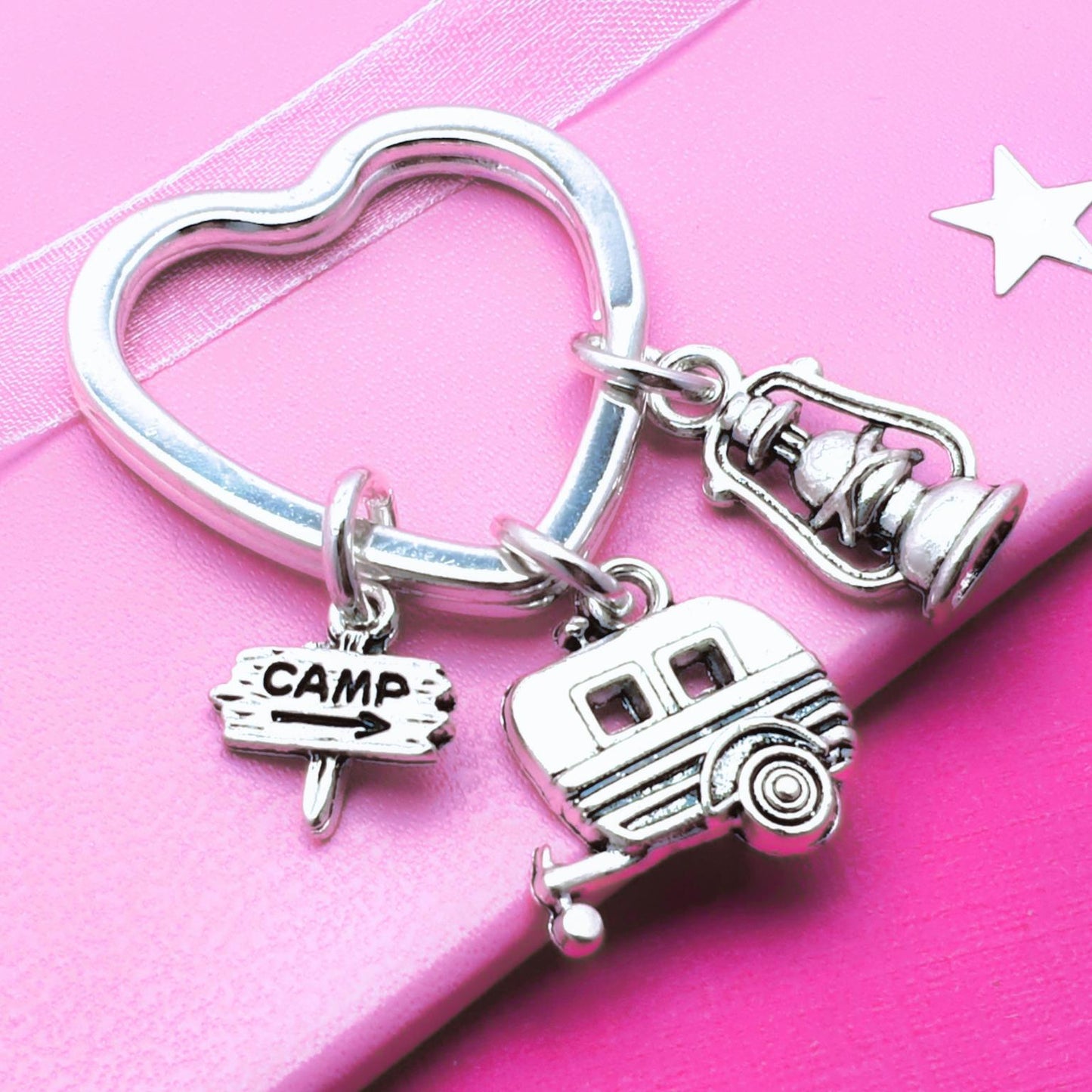 Silver keychain with various camping charms , 'CAMP' sign, and camper charm on a pink background.