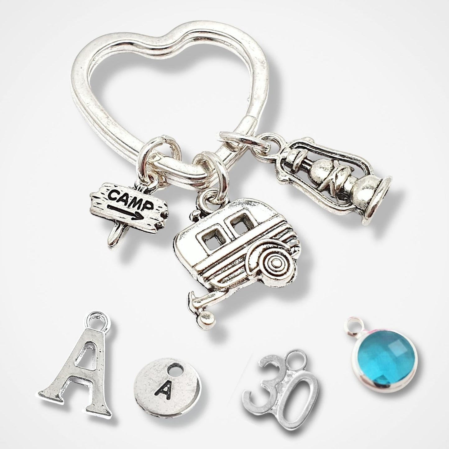 Silver keychain with various camping charms , letter 'A', number '30', and blue gemstone on a white background.
