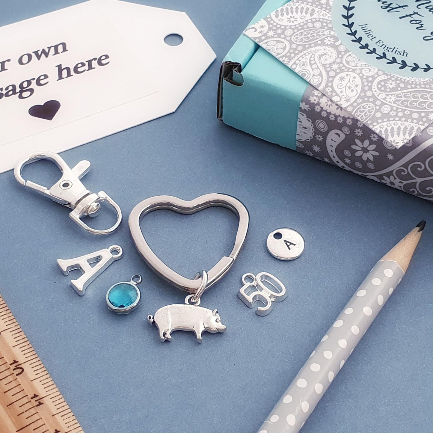 Silver pig keychain on a blue surface with packaging and a pencil.