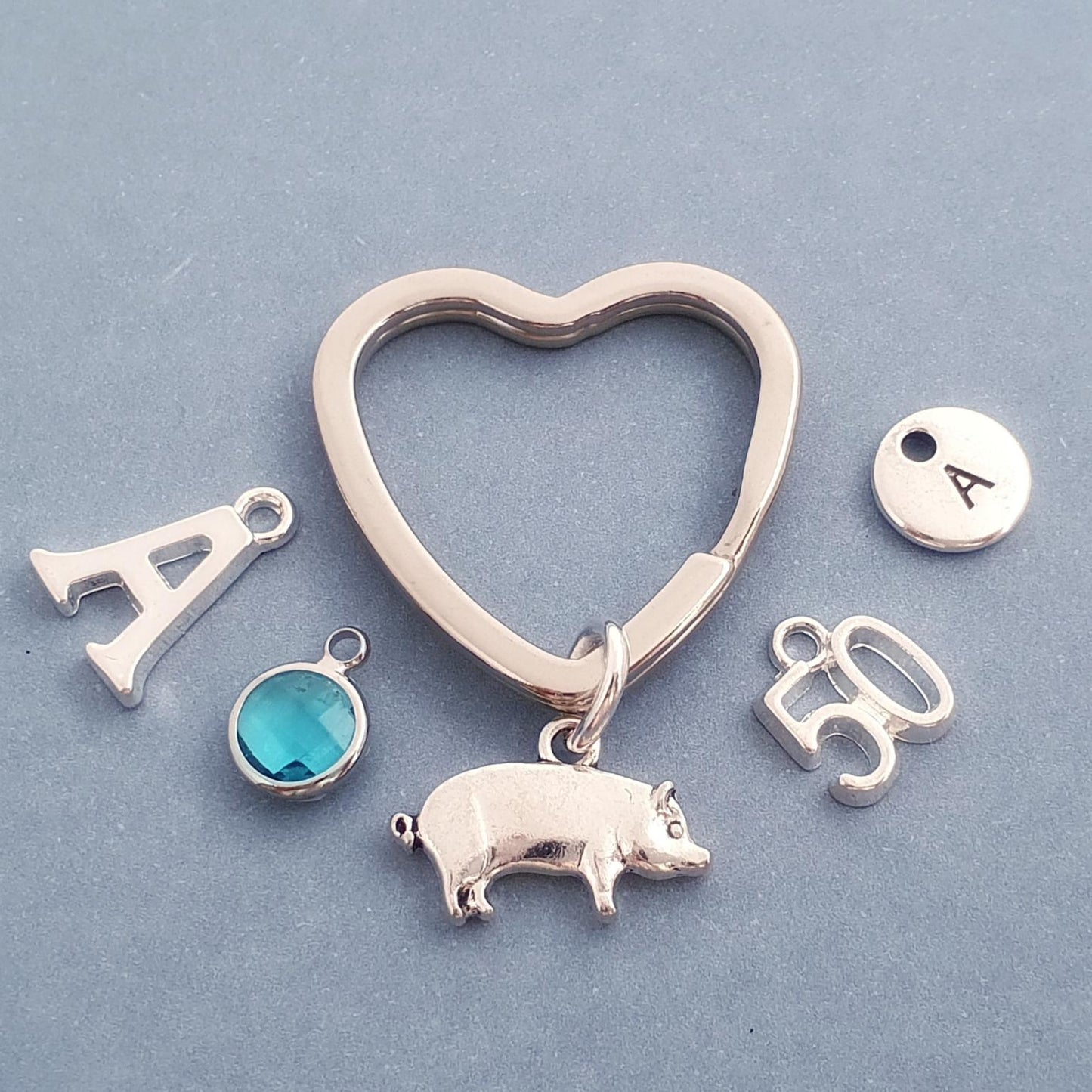Silver heart-shaped pig keychain with various charms on a light blue background