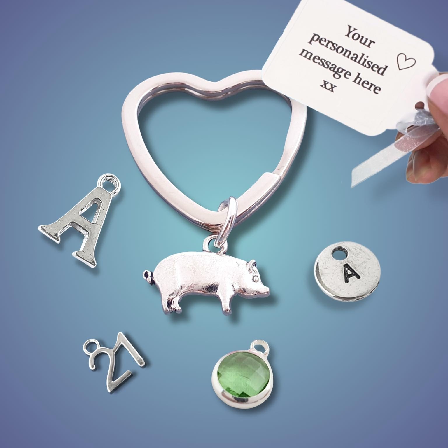 Silver keychain with pig and various charms and a hand holding a personalized message card against a blue background.