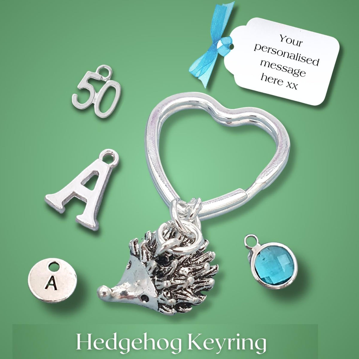A silver hedgehog keyring with a heart-shaped ring, shown with several customizable charm options on a green background. The charms include a silver number 50, a silver letter A, a silver letter A with a dot, a silver round charm with an A, and a silver hedgehog.