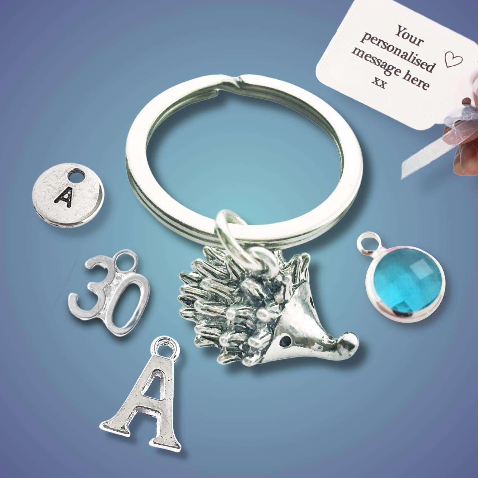 Silver keychain with hedgehog charm, letter 'A' charm, and blue gemstone on a blue background.