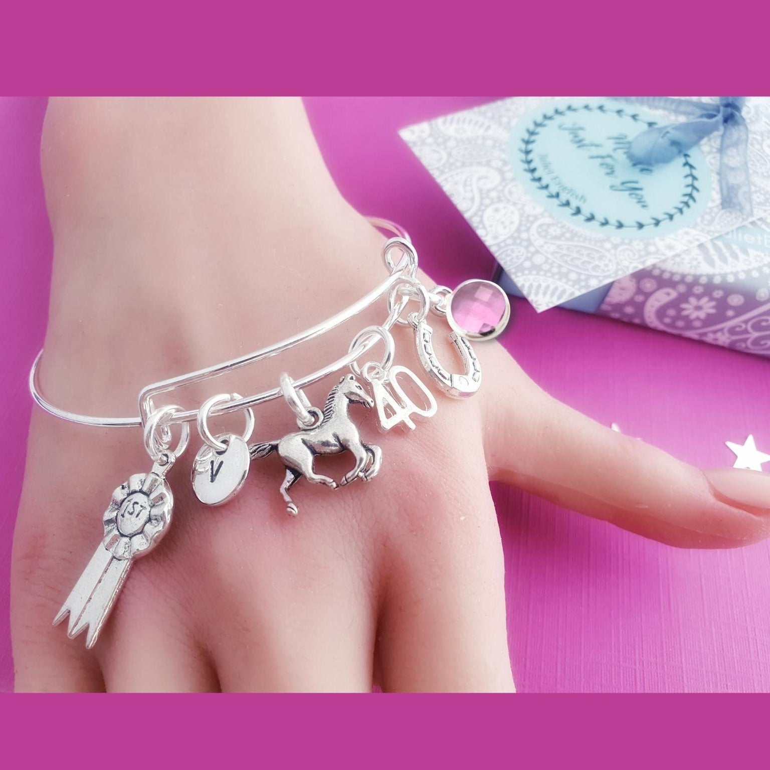 Silver bracelet with horse charms on a hand against a pink background