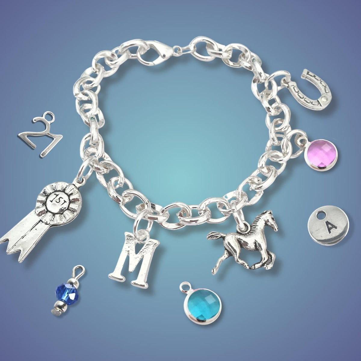 A silver charm bracelet with multiple equestrian and personalization charms, including a horse, rosette ribbon, letter 'M', horseshoe, and gemstone accents, displayed on a blue gradient background.
