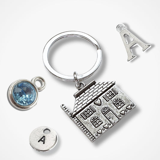 Silver keychain with house-shaped charm, blue gemstone, and letter 'A' charms on a white background