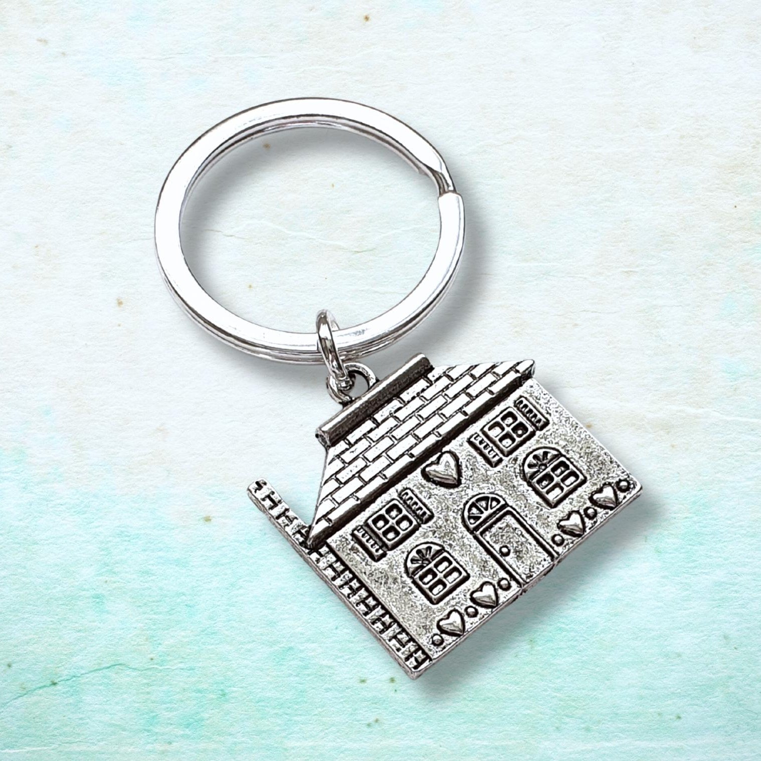 Silver keychain with house design on a light blue background